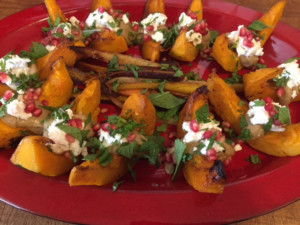 roasted kabosha squash topped with mint and pomegranate on a red platter.